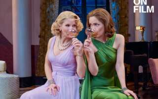 Two women in evening gowns holding wine glasses.