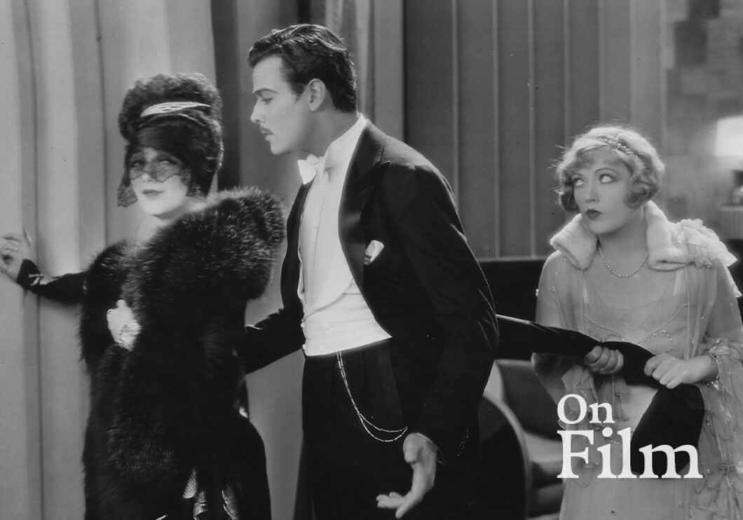 Black-and-white still frame from "The Cardboard Lover" of two women and a man in formal attire.