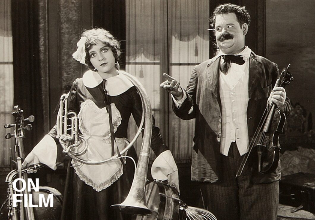 Black-and-white still of Oliver hardy next to a woman holding instruments.