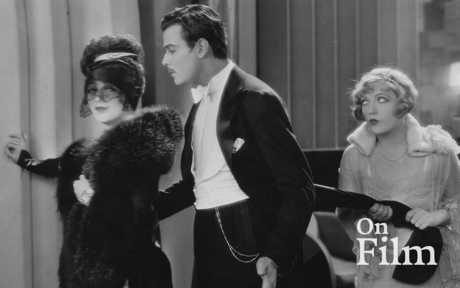 Black-and-white still frame from "The Cardboard Lover" of two women and a man in formal attire.