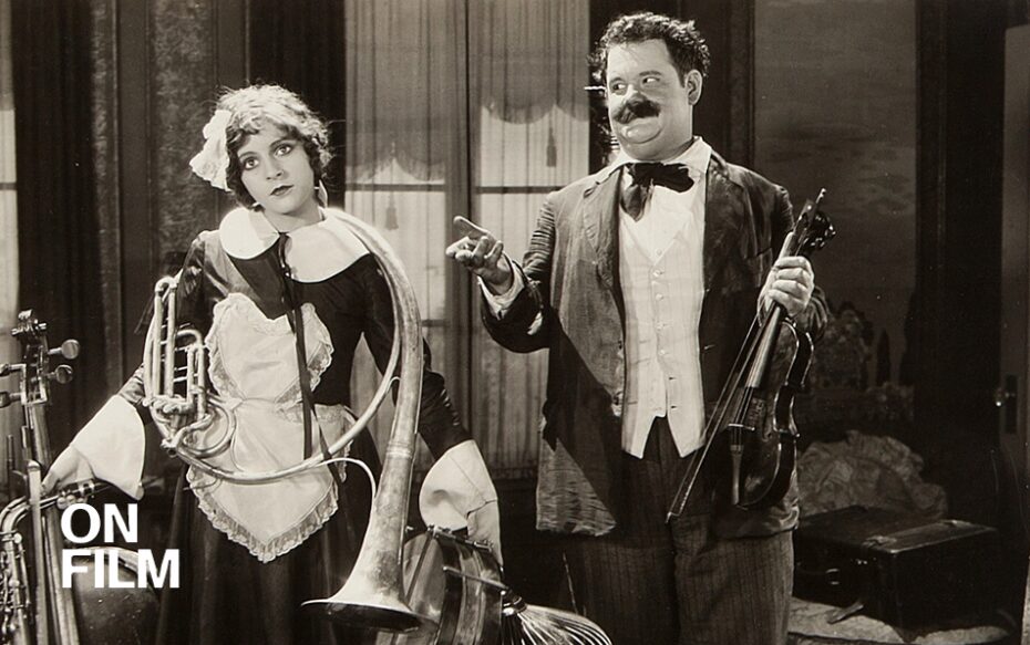 Black-and-white still of Oliver hardy next to a woman holding instruments.