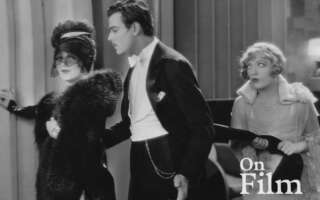 Black-and-white still frame from "The Cardboard Lover" of two women and a man in formal attire.