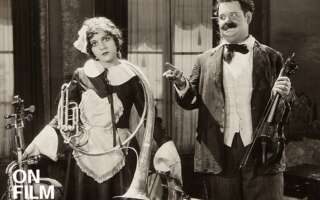 Black-and-white still of Oliver hardy next to a woman holding instruments.