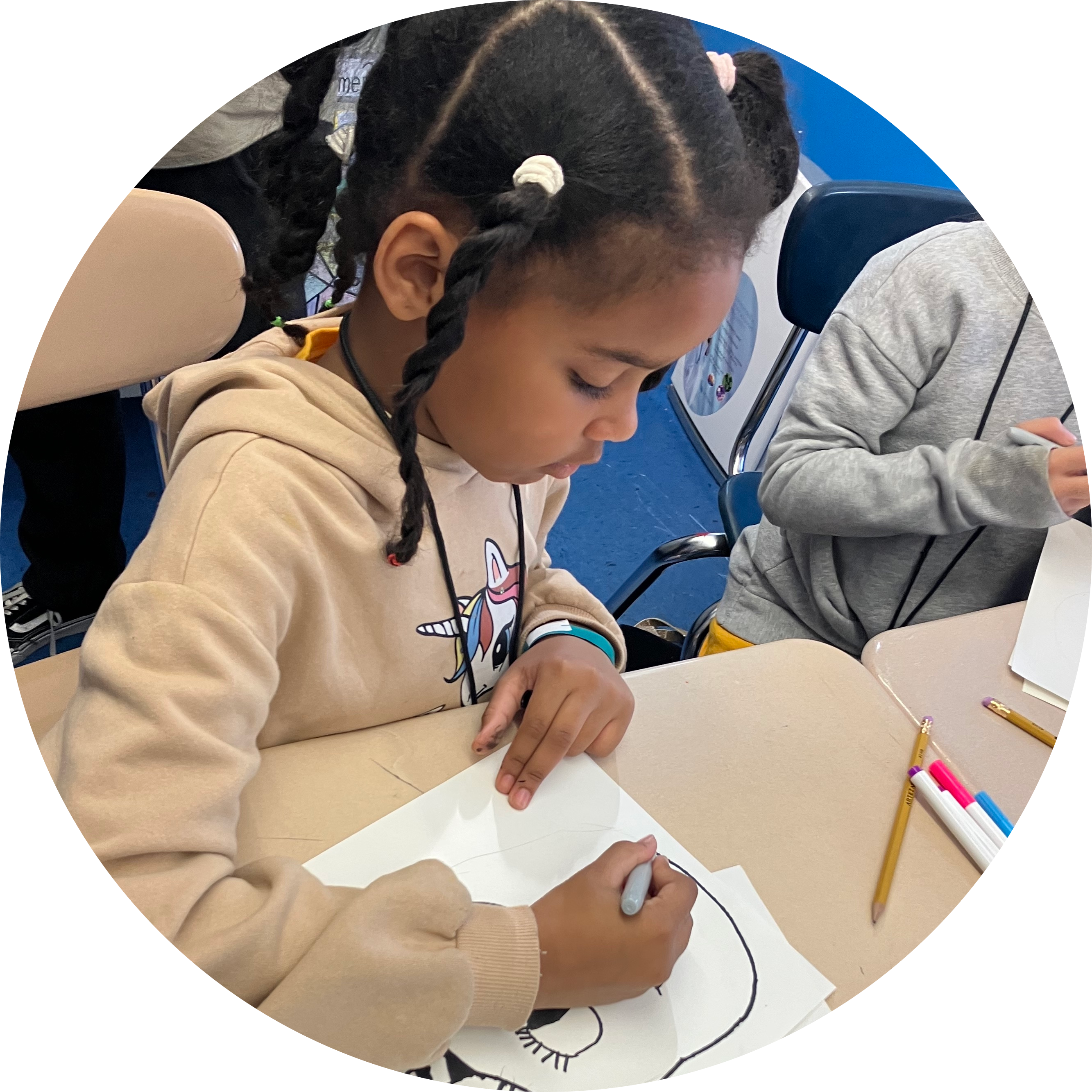 Young student sits at her desk and draws picture of a face during Global Arts visual art workshop.