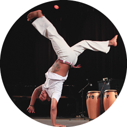 Capoeirista presents capoeira body moves, photographed in a handstand with legs split in the air.