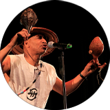 An artist performs on the stage, wearing a hat and holding two instruments.