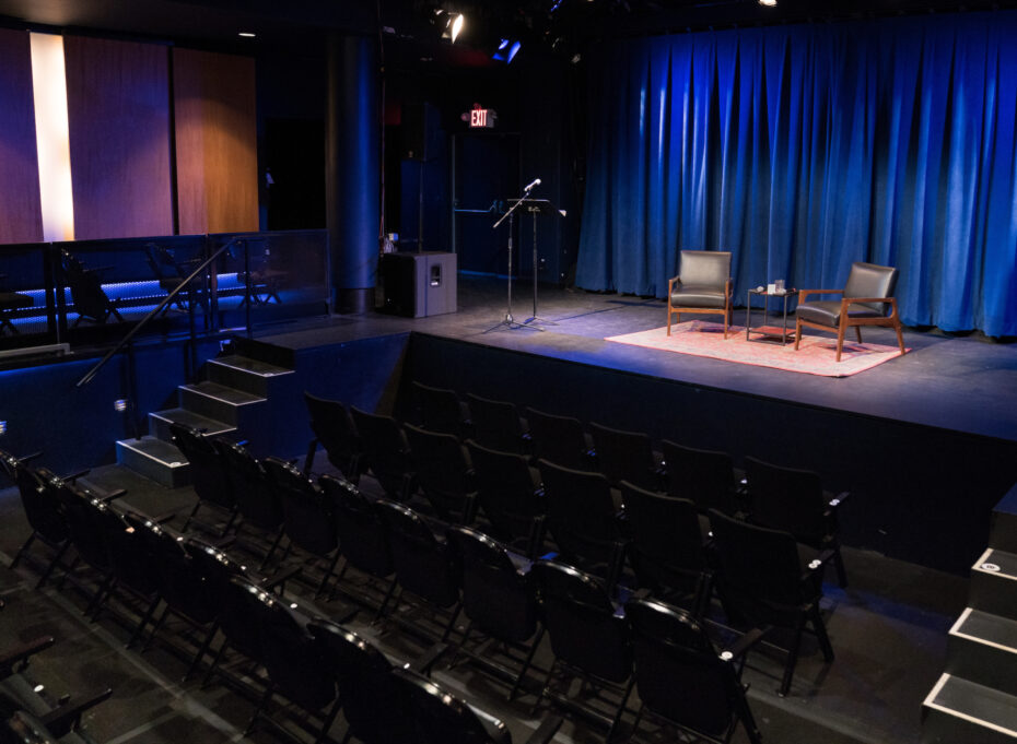 An empty theater and stage with two sitting chairs and a carpet.