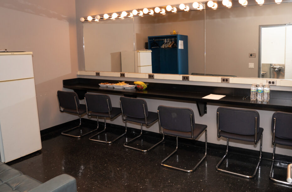 Six chairs are placed in front of a lightbulb-framed mirror in the Leonard Nimoy Thalia dressing room.