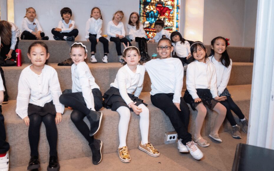 A small group of choir members seated on two benches. They all wear white shirts and black pants.