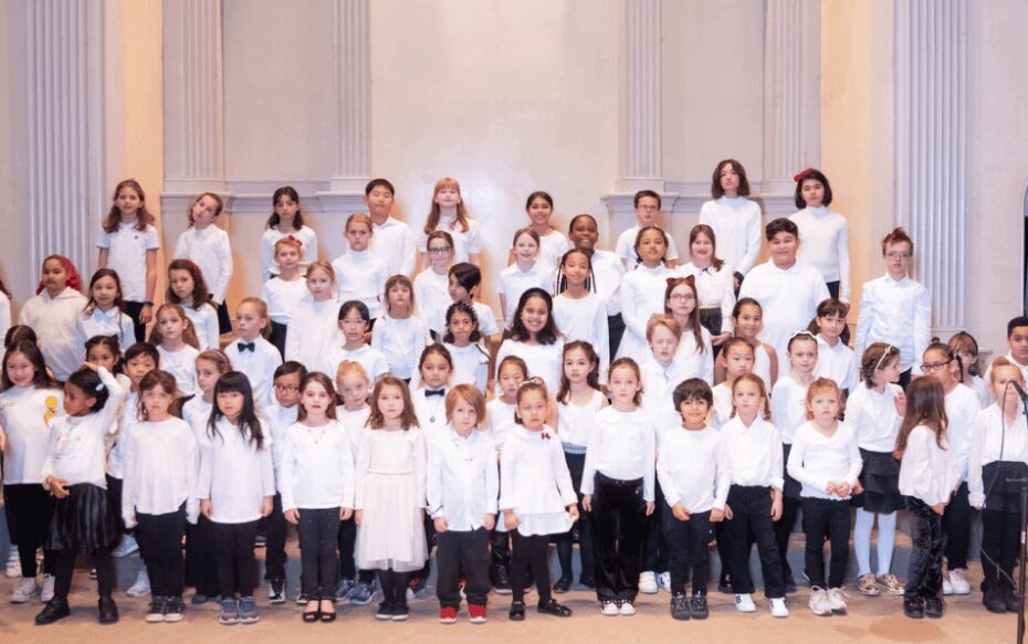 An ensemble of choir members pose for a group photo. They all wear white shirts.