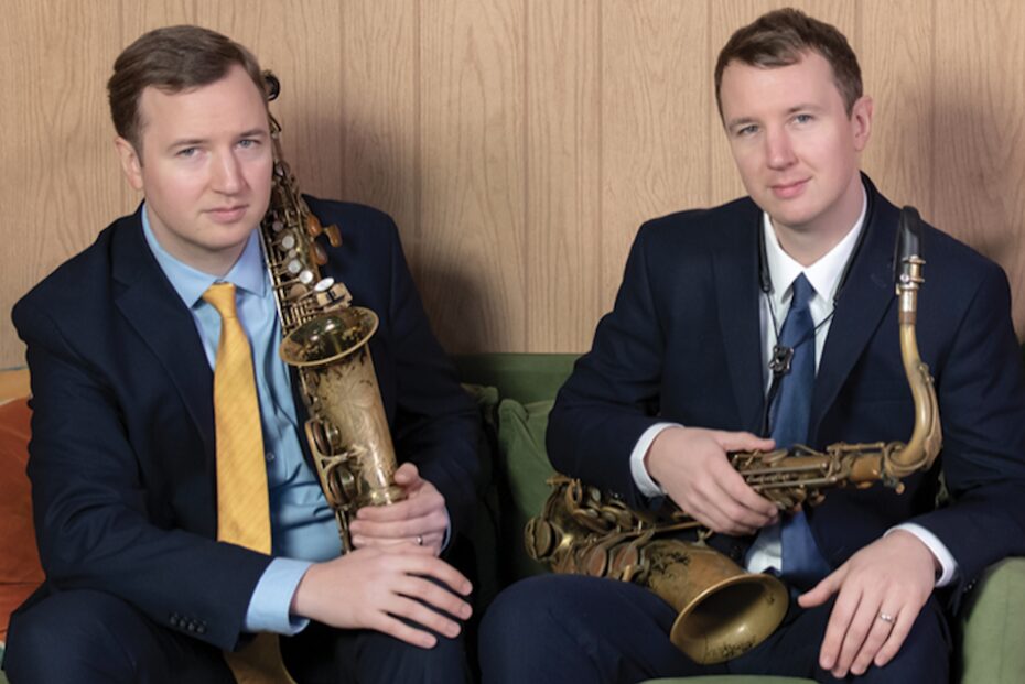 Posed promotional photo of the Anderson twins. They wear suits and hold their instruments.