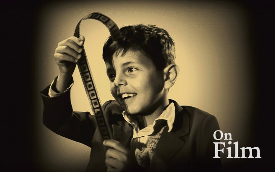 A black and white image of a boy looking at a piece of film.