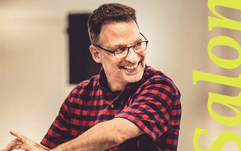 Joel Fram smiles as he conducts, with 'Salon' written in yellow lettering.