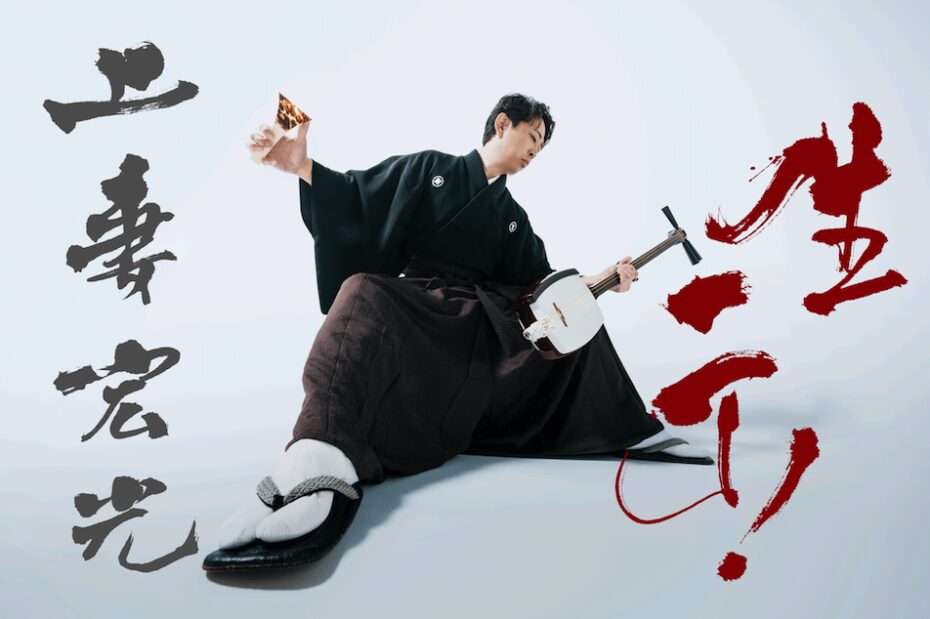 Shamisen musician Hiromitsu Agatsuma poses with shamisen in hand. The photo is shot from a low angle against a white background stylized with black and red kanji characters.