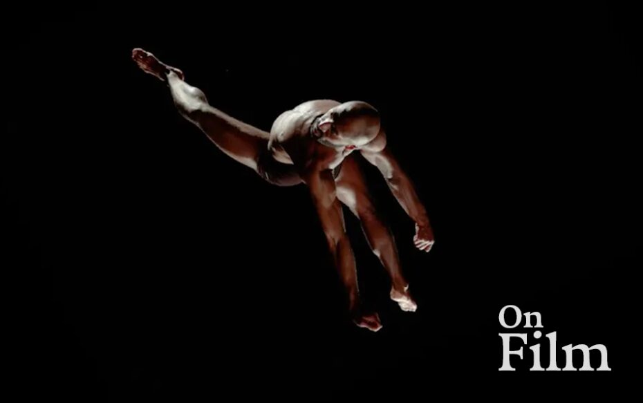 A dancer contorts their body in darkness.