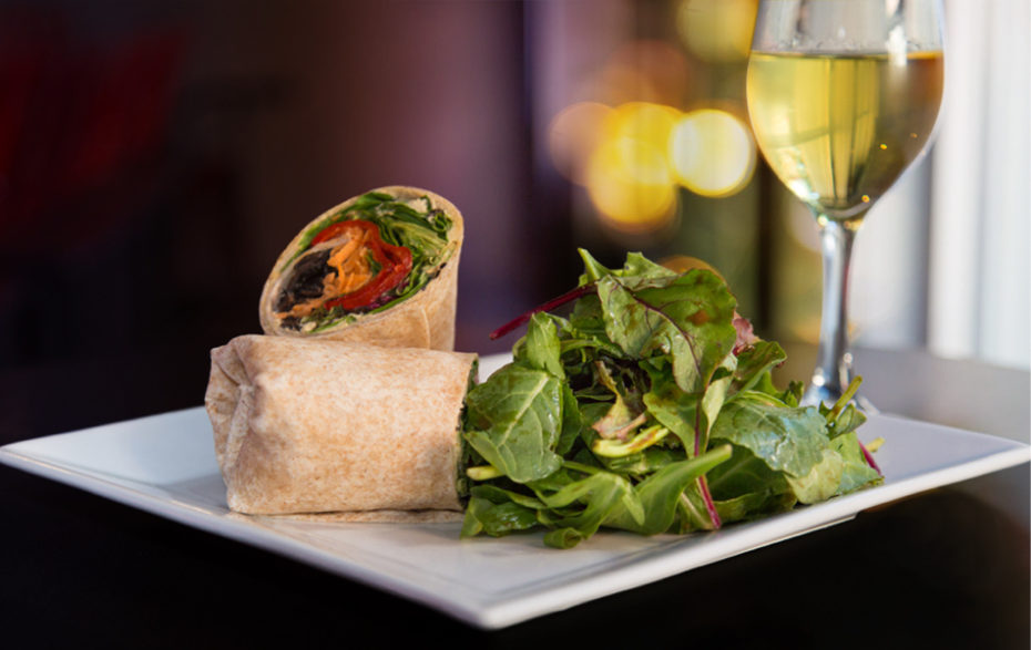 A vegetable wrap cut in half with a side salad on a plate next to a full lass of white wine.