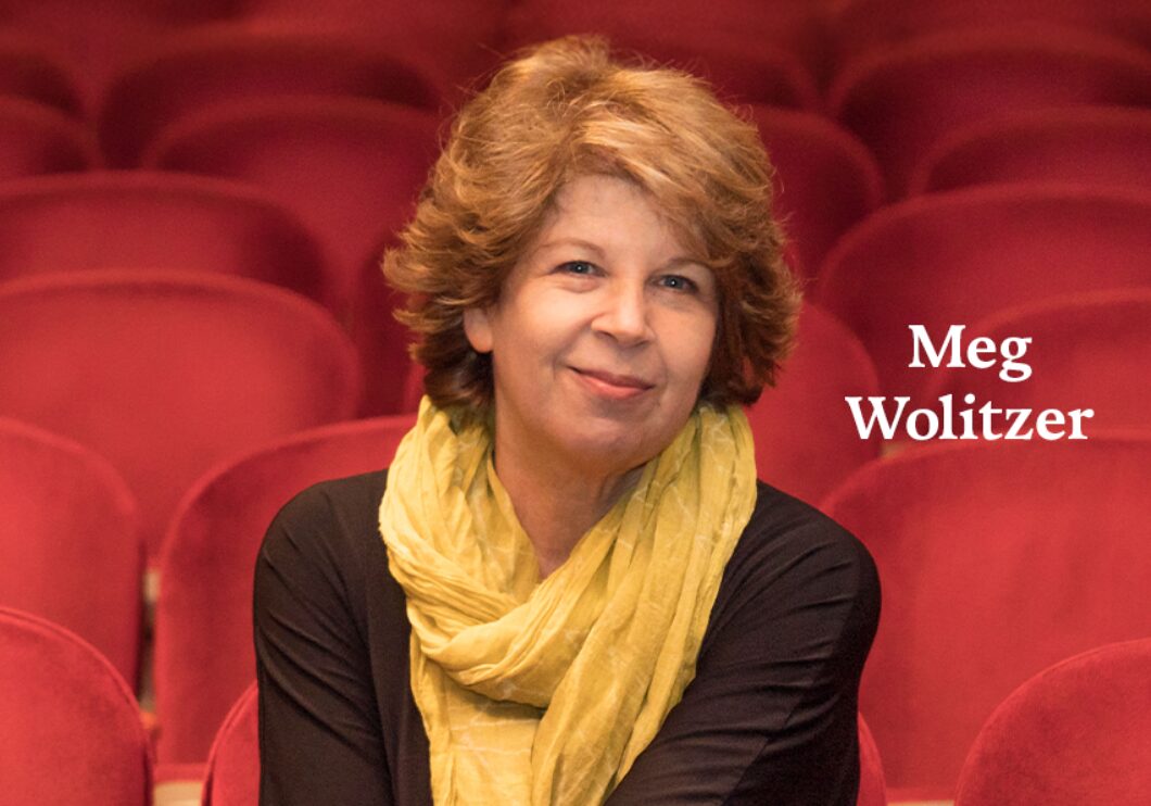 A headshot of author Meg Wolitzer, seated in a theater of red-upholstered seats. The author's name appears in white text on the right side of the image.