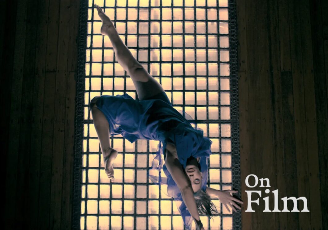 A dancer sprawled in front of a grate with light shining through.