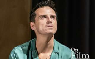Actor Andrew Scott performing in Vanya. He is wearing a blue shirt and a gold necklace.