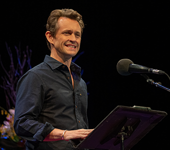 An actor reads a story in front of a music stand.