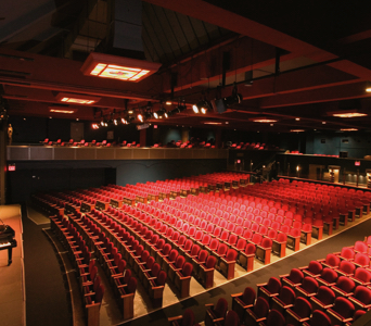 An empty Peter Jay Sharp Theatre with rows of red velvet seats as seen from the side balcony.
