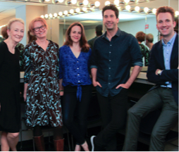 Five actors stand in front of a dressing room mirror smiling.