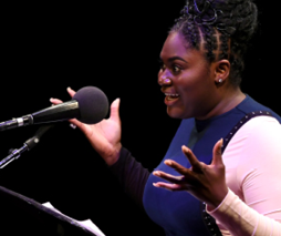 Danielle Brooks reads on the stage with expressive upraised hands