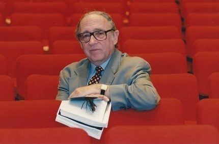Isaiah Sheffer sitting in the red seats of the empty Sharp Theatre.
